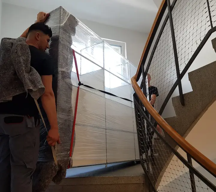 Zügelmänner tragen ein verpacktes schweres Möbelstück durch das Treppenhaus