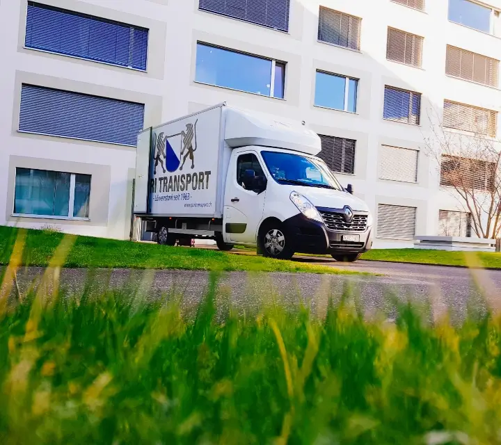 Umzugswagen von Züri Transport hinter einer Wiese